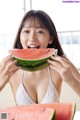 A woman in a white bikini eating a slice of watermelon.