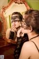 A woman wearing a black lace mask looking at herself in the mirror.