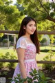 A woman in a pink dress standing next to a tree.