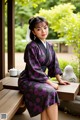 A woman in a purple and black kimono sitting on a bench.