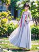 A woman in a long white dress standing in front of a tree.