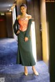 A woman in a long green dress standing in a hallway.